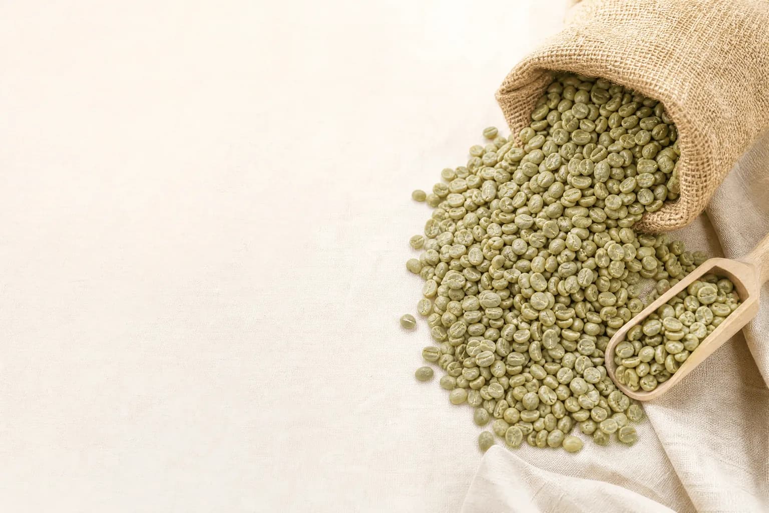 An open jute sack spilling raw green Tanzanian coffee beans
